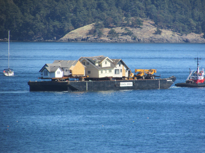a barge carries a large home across the sea