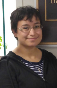 Headshot of young woman with short dark hair, glasses, with striped shirt