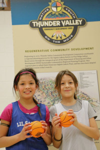 Two young Lakota girls in athletic gear and holding small basketballs smiling
