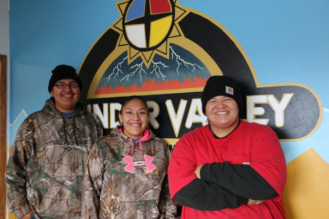Three young adults smile in front of a Thunder Valley CDC sign